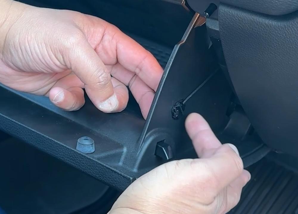 Hands disconnecting the damper cord from the Dodge Ram glove box, demonstrating Step 2 of the Dust Armor CAFDA-R01 cabin air filter replacement process.