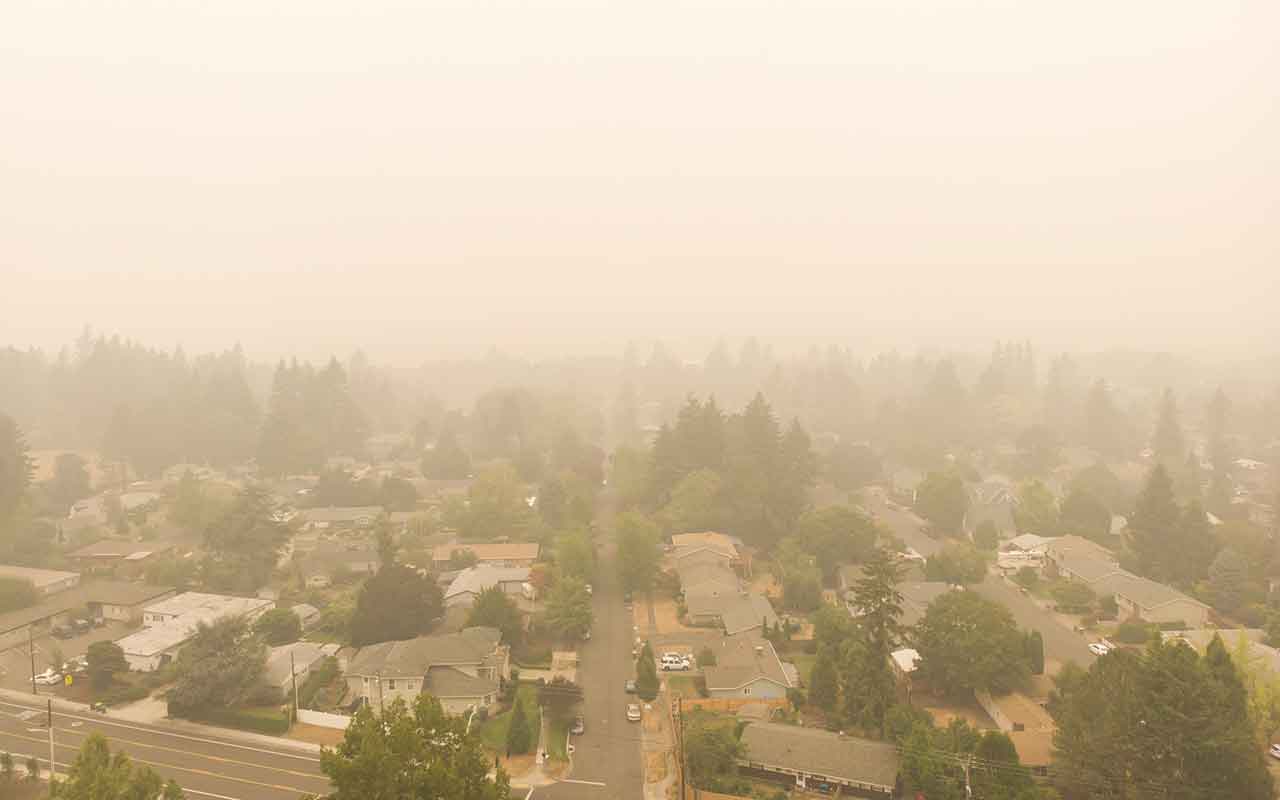 Suburban neighborhood covered in dense wildfire smoke reducing outdoor air quality, an aerial view of homes and streets in heavy haze
